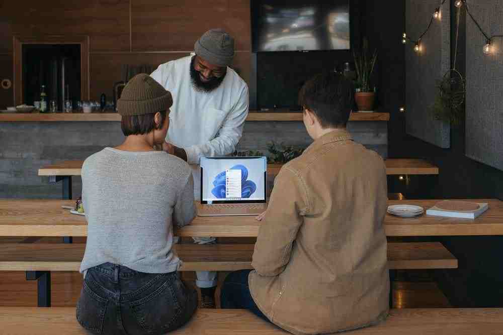 Three people sitting on benches at work around a Microsoft laptop 